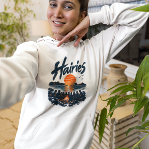 Young woman posing for a selfie indoors, wearing a white hoodie with a sunset graphic and blue jeans.