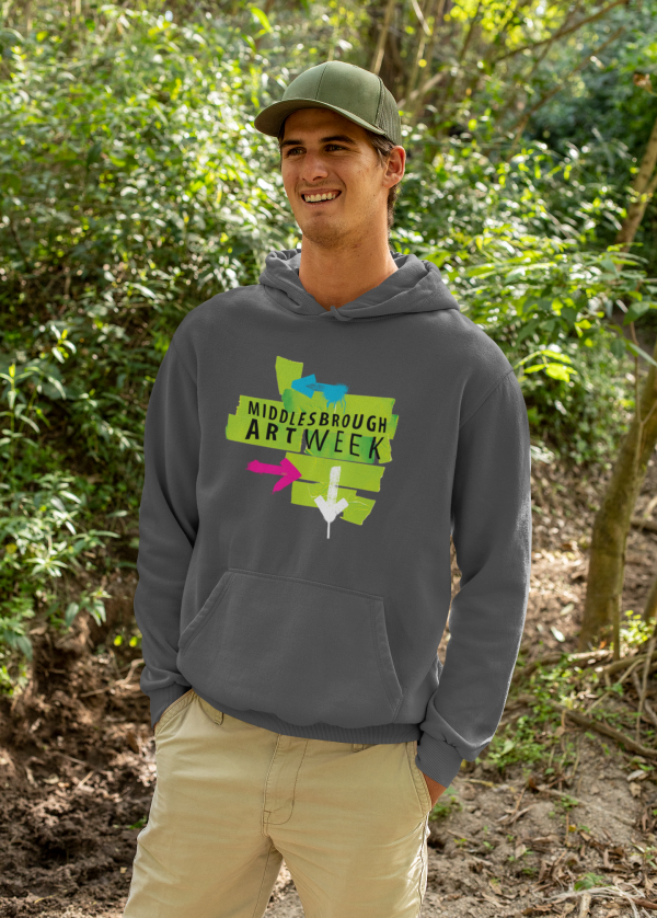 Custom Printed T Shirts - The T Shirt Man 3 โ The T Shirt Man | Next Day T Shirt Printing & Custom Hoodies Smiling man outdoors in a forested area, wearing a gray hoodie with a bright Middlesbrough Art Week graphic on the front.